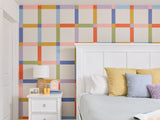 Felt Right wall art design in a bedroom with a plaid design using pink, orange, green, and blue felt tiles behind a bed and a night stand.