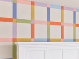 Felt Right wall art design in a bedroom with a plaid design using pink, orange, green, and blue felt tiles behind a headboard of a bed.