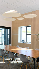 Four cream-colored flat circular ceiling baffles suspended at varying heights above a conference table in an office setting.