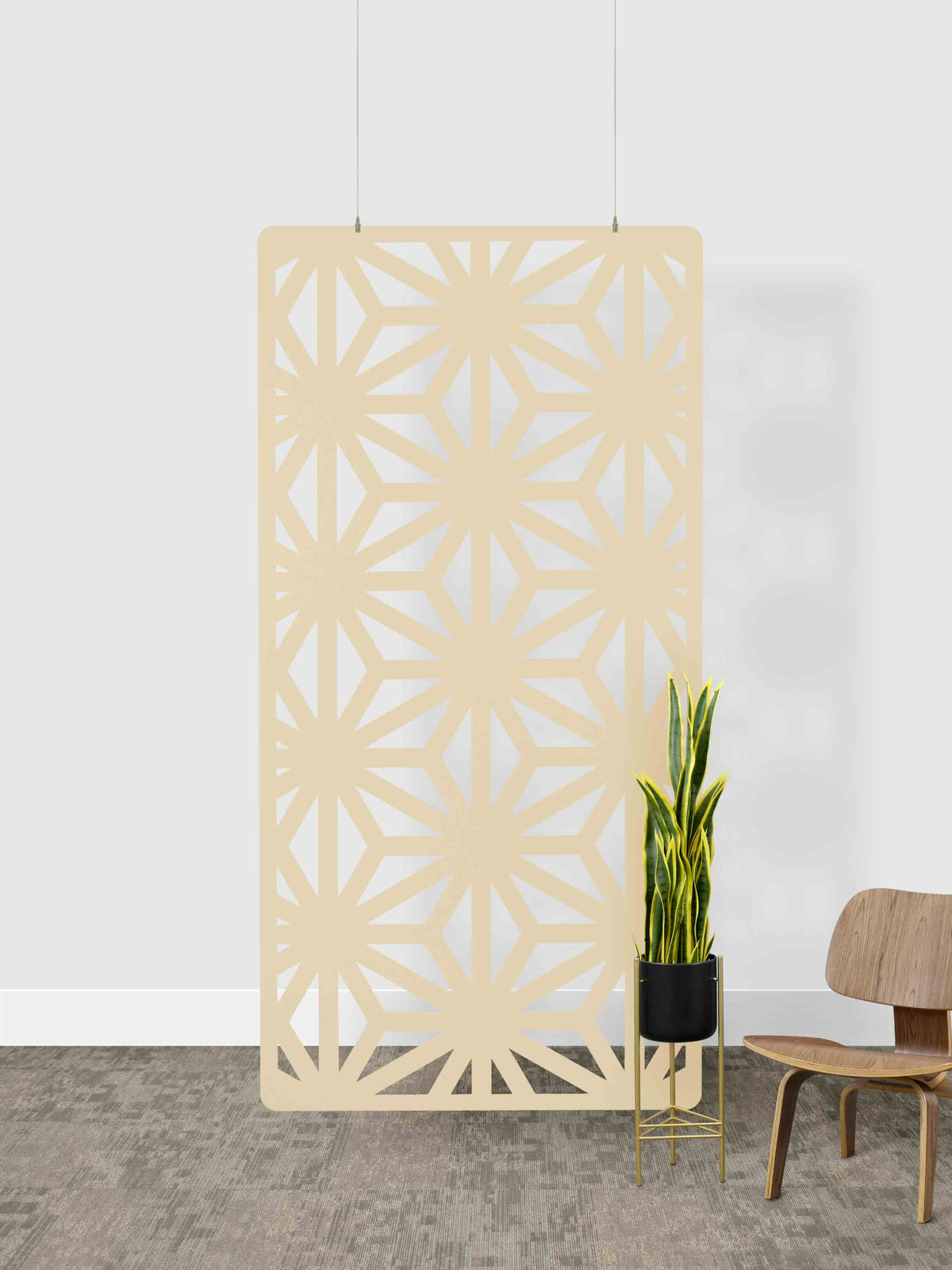 Decorative screen with geometric pattern next to a plant and chair against a white wall