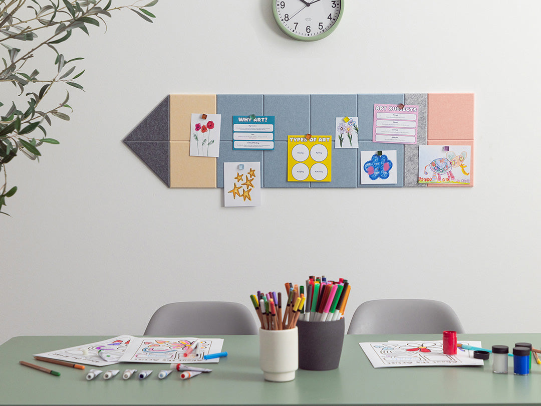 Children's art display on a wall with a table in front featuring art supplies.
