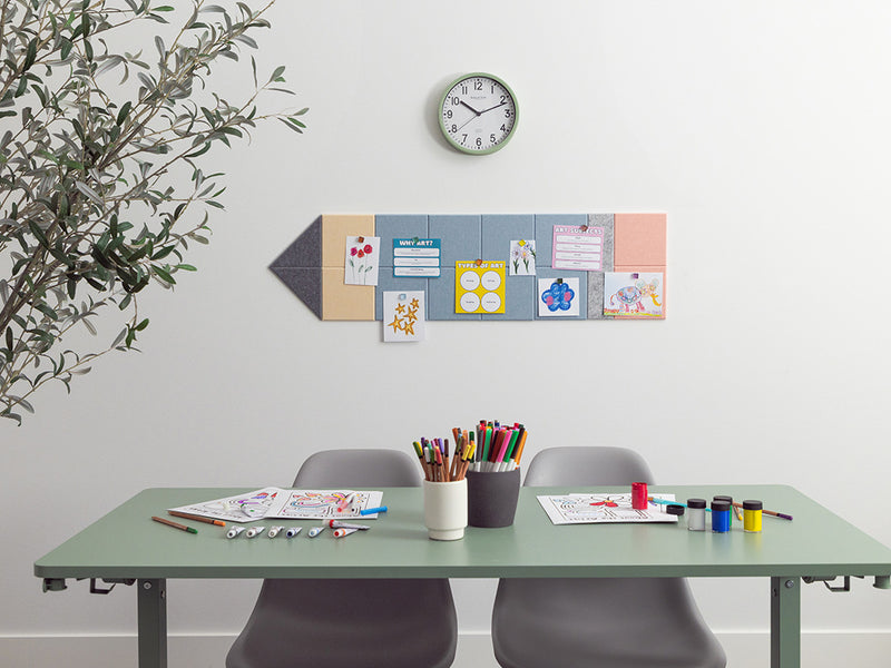 Desk with art supplies, chairs, and a wall with a clock and decorative items.