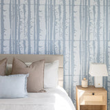 A styled bedroom scene featuring a bed with neutral-toned bedding and decorative pillows, set against a wall with vertical birch tree pattern wallpaper.