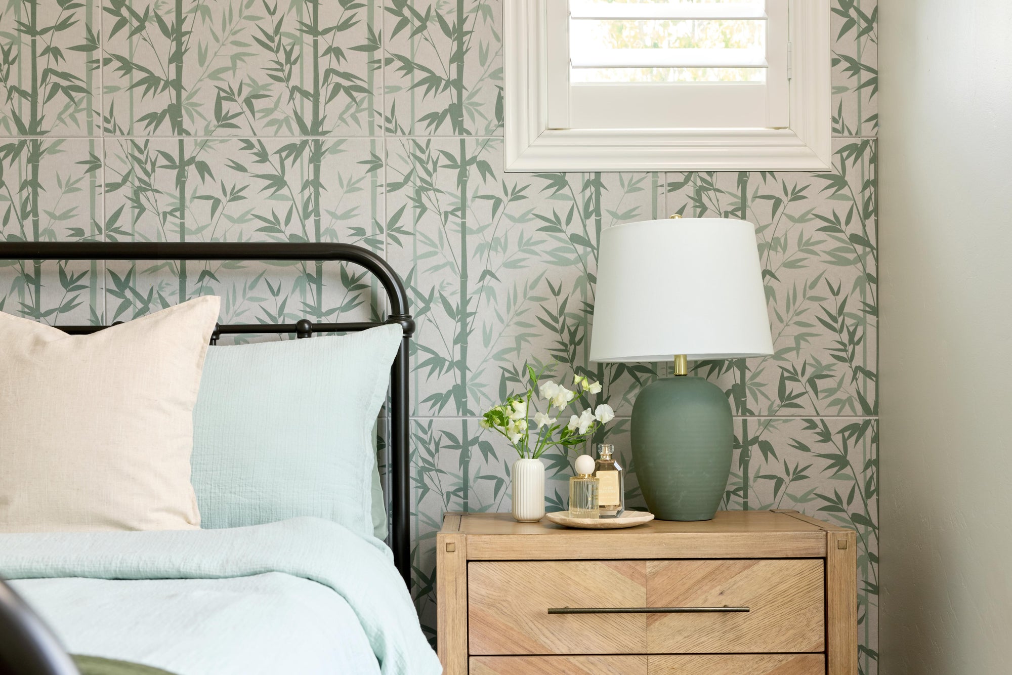 Bedroom with floral wallpaper, bed with pillows, wooden nightstand, and lamp.