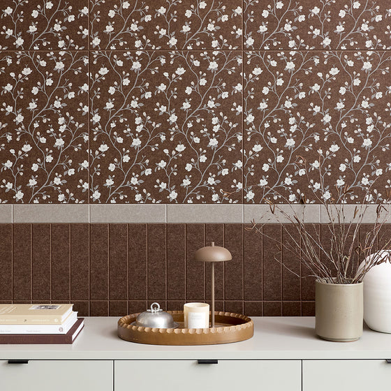 Brown floral patterned wall tiles with a white vine and blossom design, shown installed on a wall above a white cabinet with decorative items.