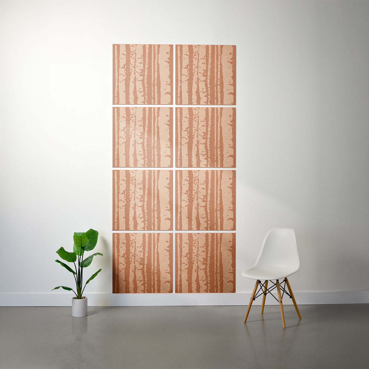 A wall art set featuring a vertical birch tree bark pattern in warm peach and brown tones, displayed on a white wall in a modern room setting with a white chair and a potted plant.