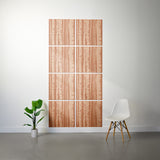 A wall art set featuring a vertical birch tree bark pattern in warm peach and brown tones, displayed on a white wall in a modern room setting with a white chair and a potted plant.