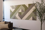 Modular wall art made of geometric triangular tiles in green, beige, and gray tones arranged in a diamond pattern above a sof