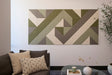 A Felt Right wall art design that is geometric artwork featuring various shades of green and beige mounted on a wall, with a sofa and pillows in the foreground.