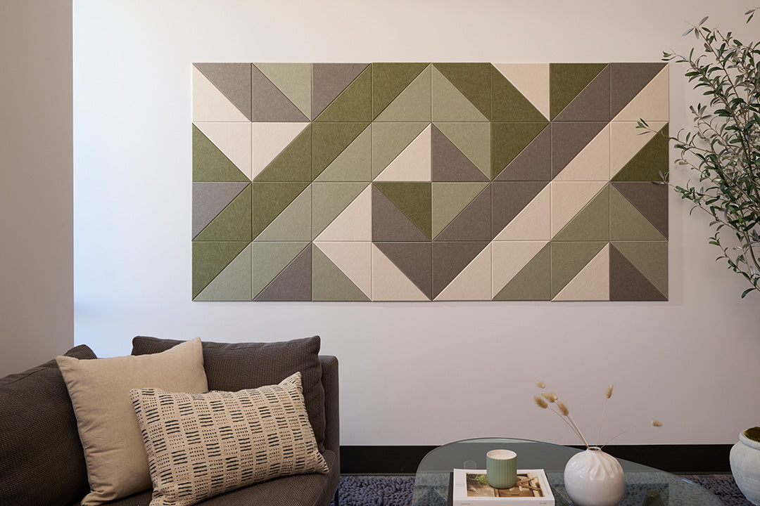 A Felt Right wall art design that is geometric artwork featuring various shades of green and beige mounted on a wall, with a sofa and pillows in the foreground.