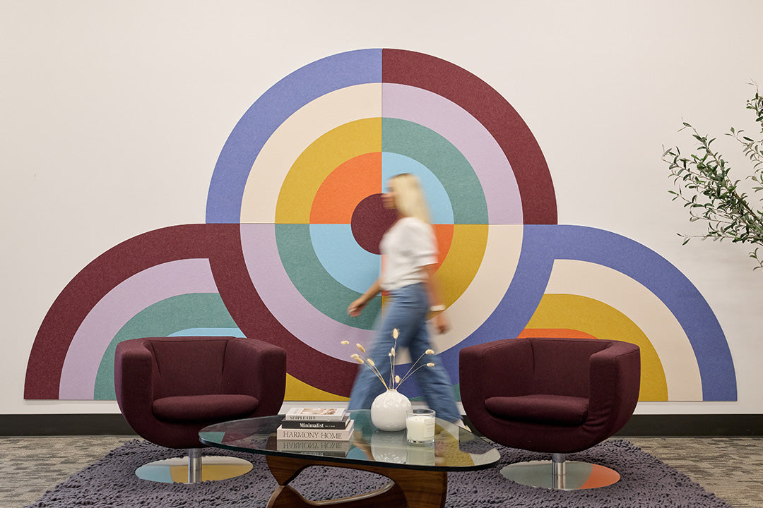 Modern waiting room with colorful abstract acoustic wall art and two dark red chairs.