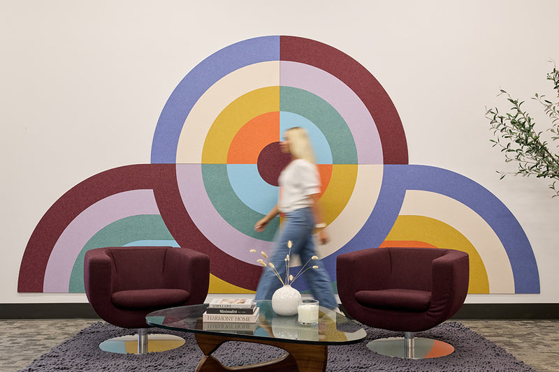 Modern waiting room with colorful abstract acoustic wall art and two dark red chairs.