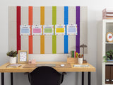 Beige cork board with alternating vertical rainbow stripes in red, orange, yellow, green, blue, and purple with five pinned c