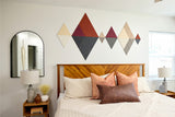 Geometric fabric wall art with cream, rust, burgundy, and charcoal diamond shapes arranged above a wooden bed.