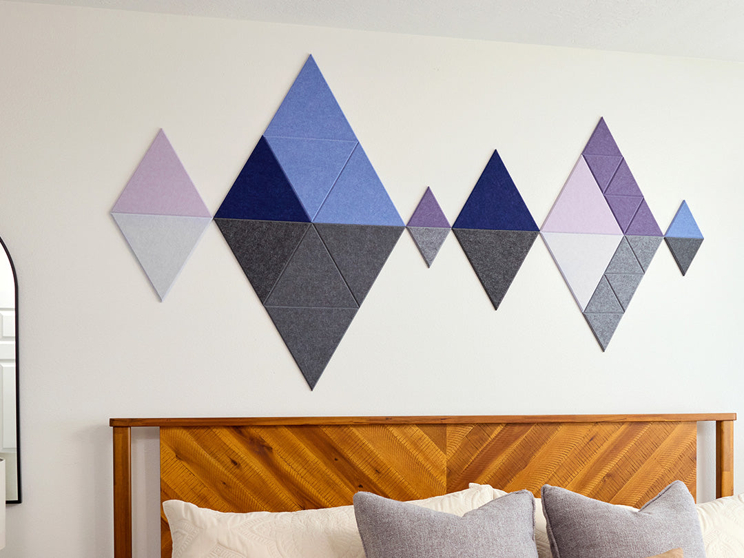 Geometric wall art with diamond shapes in various shades of purple and gray above a wooden headboard.