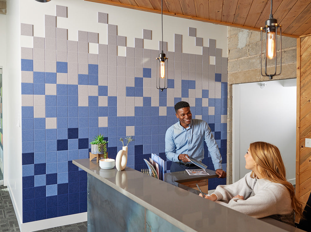 Two people at a receptionist desk talking with a blue wall design behind them.