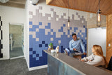 A Felt Right wall art design using pixelated tiles in an ombre pattern in shades of blue and gray in an office next to a check-in desk and two people talking