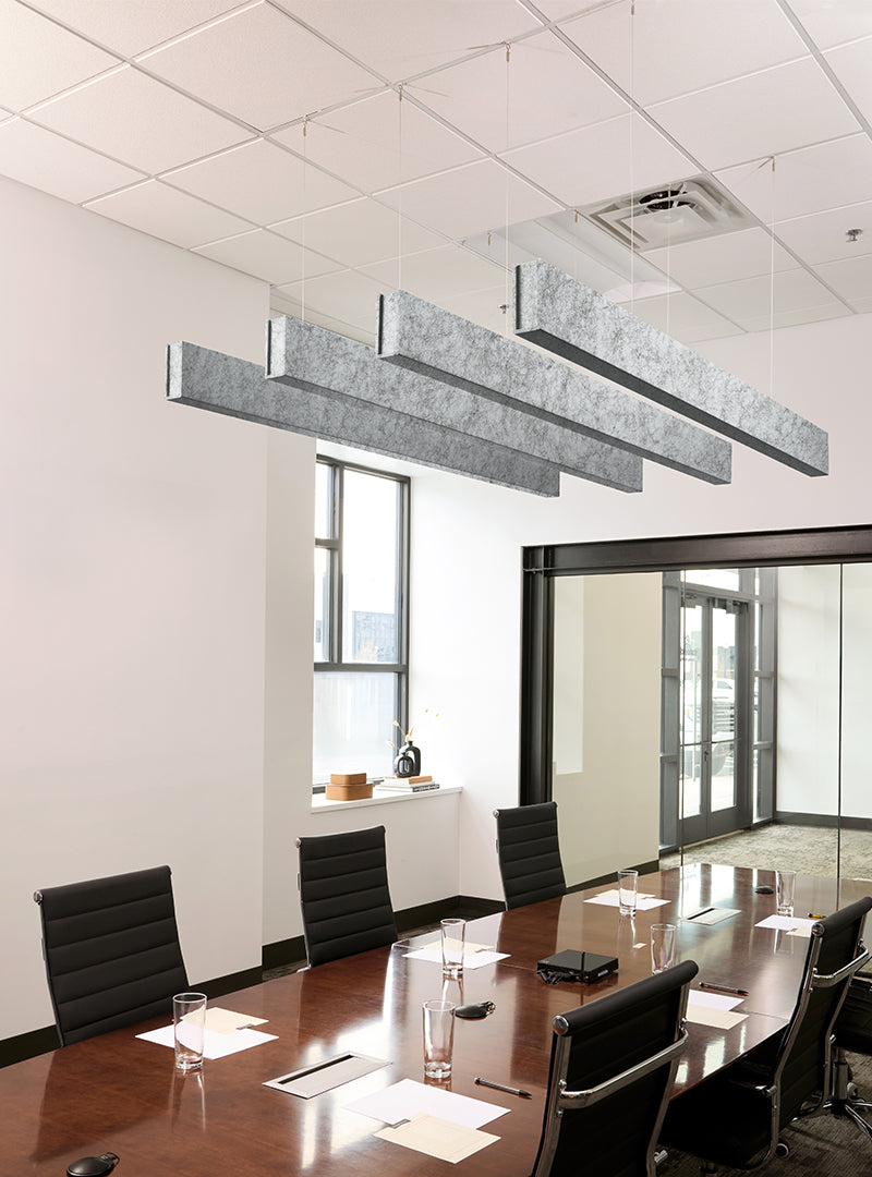 Modern office meeting room with a long wooden conference table, black office chairs, large rectangular suspended ceiling light fixtures, and glass walls.
