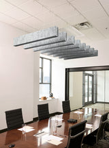 A modern conference room with a long wooden table, black office chairs, and a large rectangular suspended light fixture with layered gray panels hanging from the ceiling.