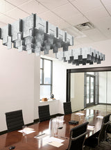 Modern office conference room with a long wooden table, black chairs, large windows, and two large geometric hanging chandeliers suspended from a white ceiling grid.