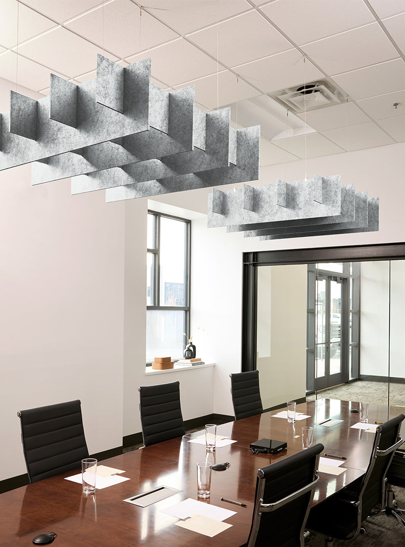 Modern office conference room with a long dark wood table, black chairs, large geometric hanging light fixtures, and glass walls in the background.