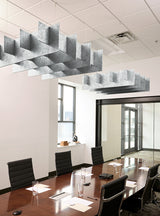 Modern office conference room with a long dark wood table, black chairs, large geometric hanging light fixtures, and glass walls in the background.