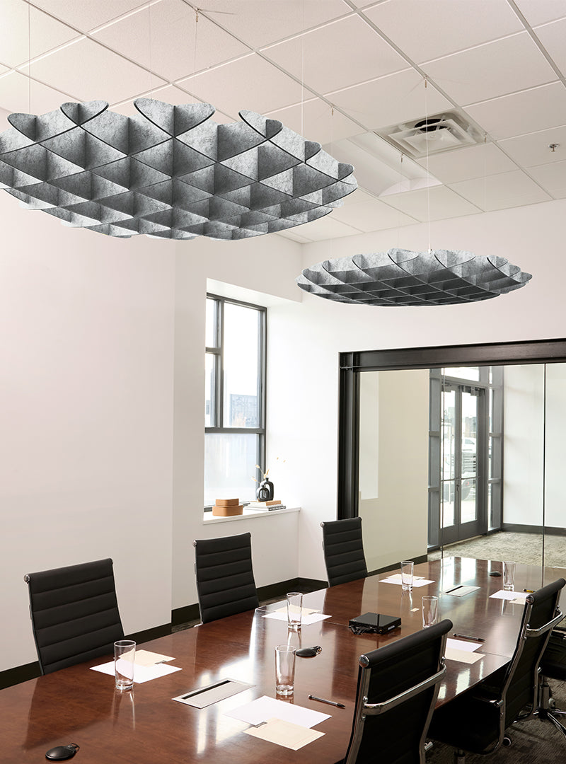 Modern conference room with a long wooden table, black office chairs, large ceiling-mounted sculptural pendant lights, white walls, and glass partition walls.