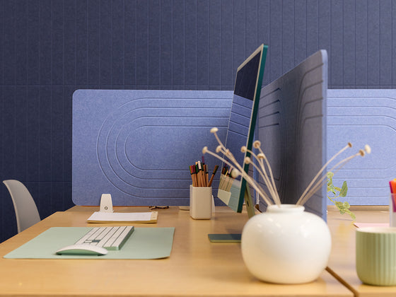 Modern office desk setup with two computer monitors, keyboard, and decorative elements against a blue wall.