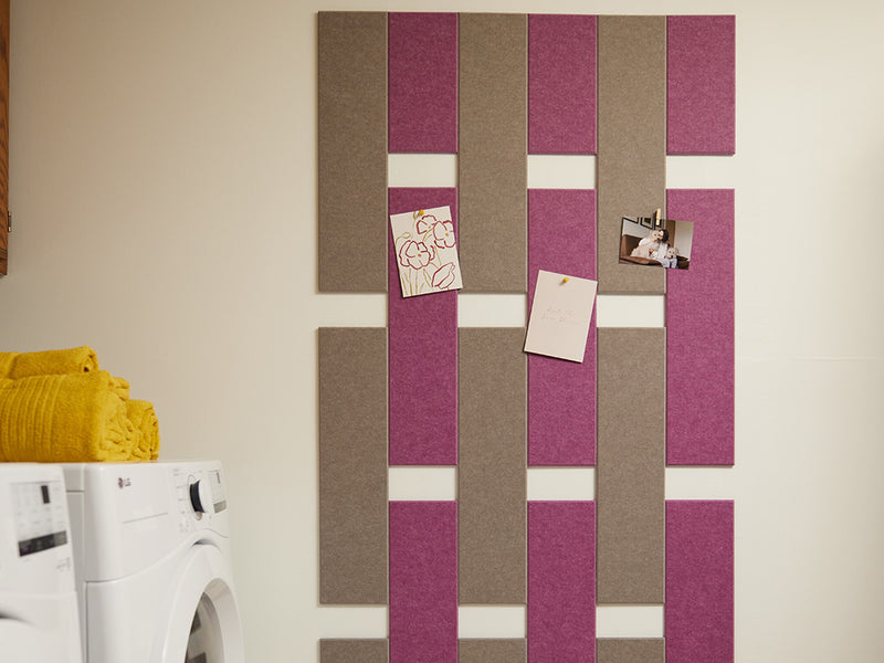 A Felt Right wall art design in shades of brown and pink felt tiles that are pinnable on a white wall in a laundry room with a washer and a dryer