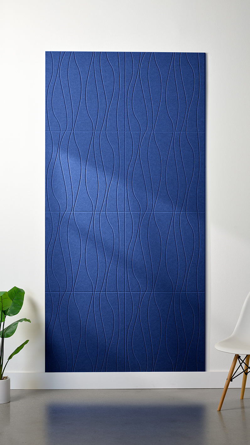 Blue Felt Right 4’ x 8’ PET felt panel with flowing lines engraved into the material against a white wall. A plant and chair are in the foreground.
