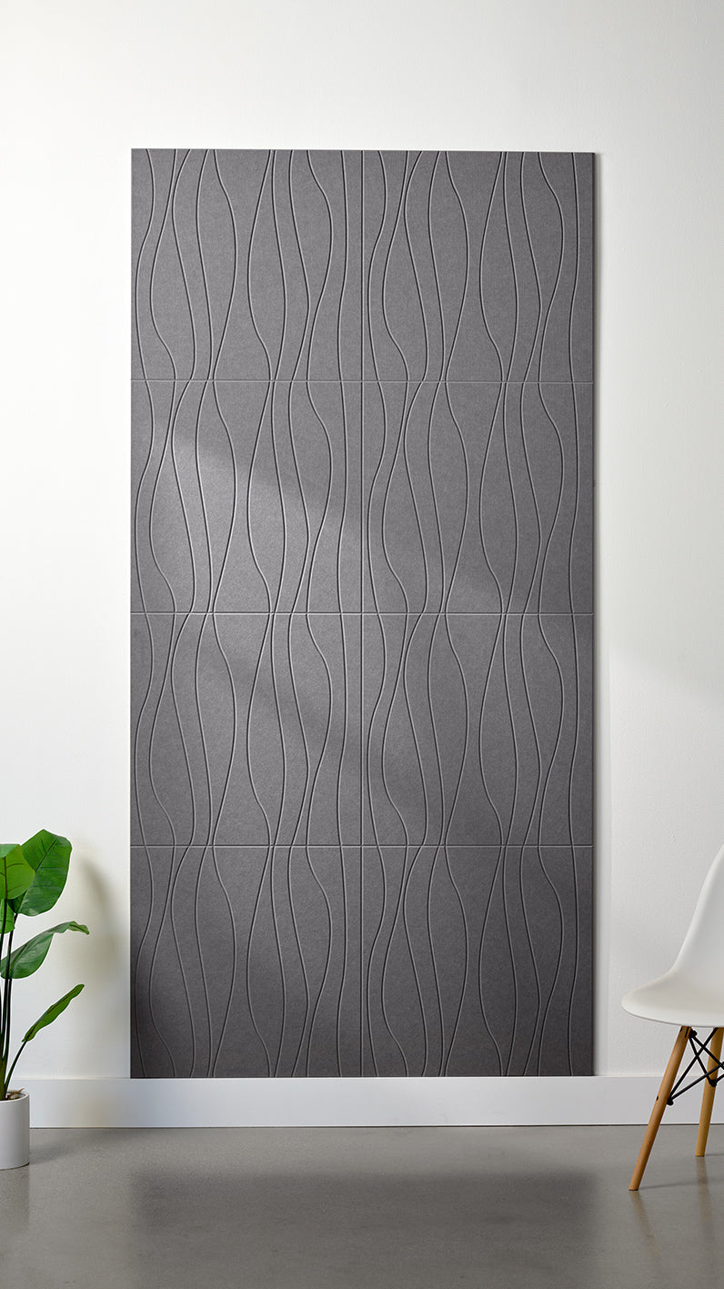 Grey Felt Right 4’ x 8’ PET felt panel with flowing lines engraved into the material against a white wall. A plant and chair are in the foreground.