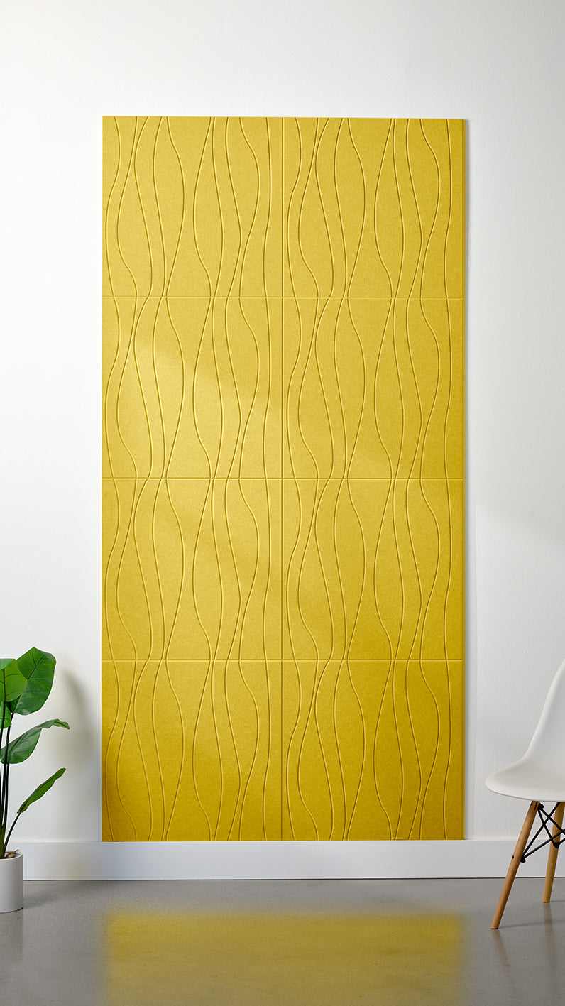 Bright yellow Felt Right 4’ x 8’ PET felt panel with flowing lines engraved into the material against a white wall. A plant and chair are in the foreground.