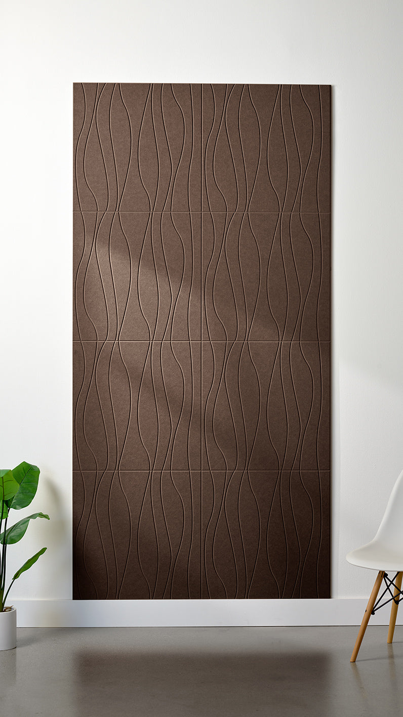 Brown Felt Right 4’ x 8’ PET felt panel with flowing lines engraved into the material against a white wall. A plant and chair are in the foreground.