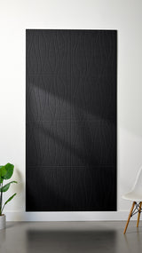 Black Felt Right 4’ x 8’ PET felt panel with flowing lines engraved into the material against a white wall. A plant and chair are in the foreground.