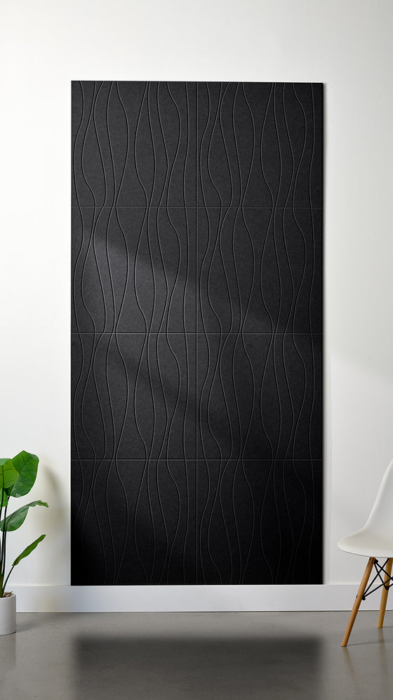 Black Felt Right 4’ x 8’ PET felt panel with flowing lines engraved into the material against a white wall. A plant and chair are in the foreground.