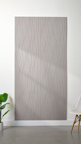 Light grey Felt Right 4’ x 8’ PET felt panel with flowing lines engraved into the material against a white wall. A plant and chair are in the foreground.