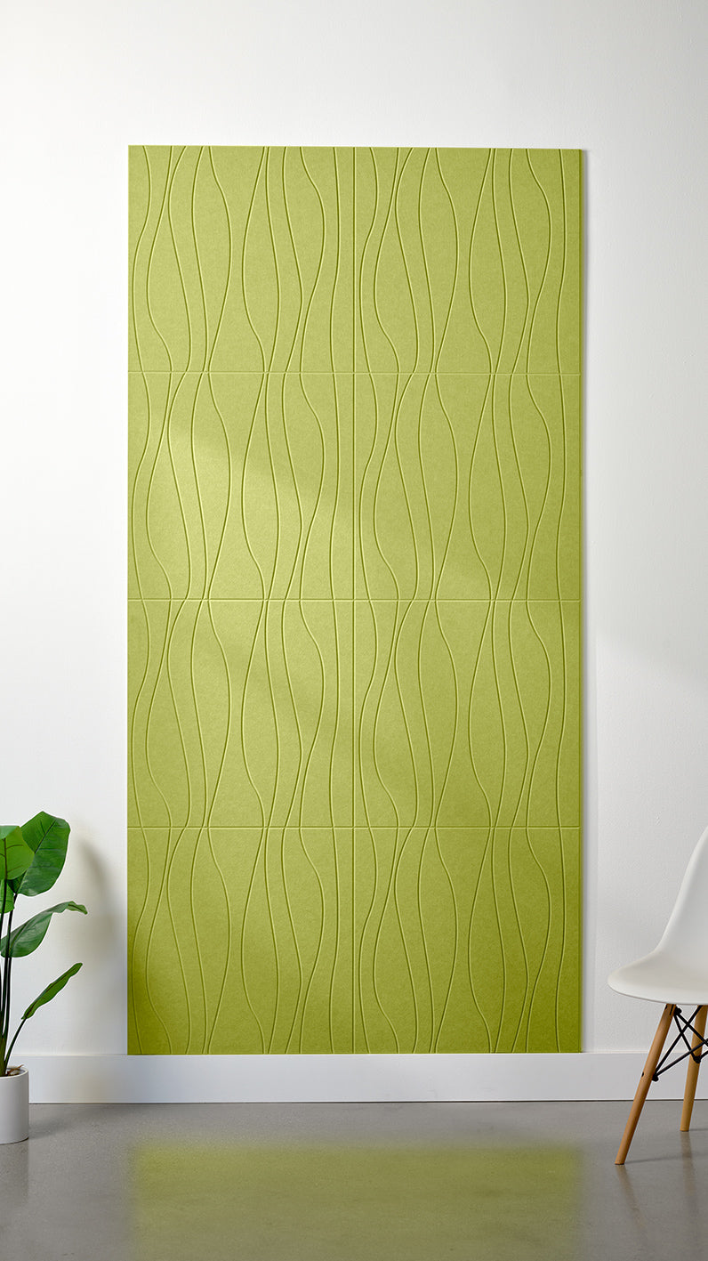Bright green Felt Right 4’ x 8’ PET felt panel with flowing lines engraved into the material against a white wall. A plant and chair are in the foreground.