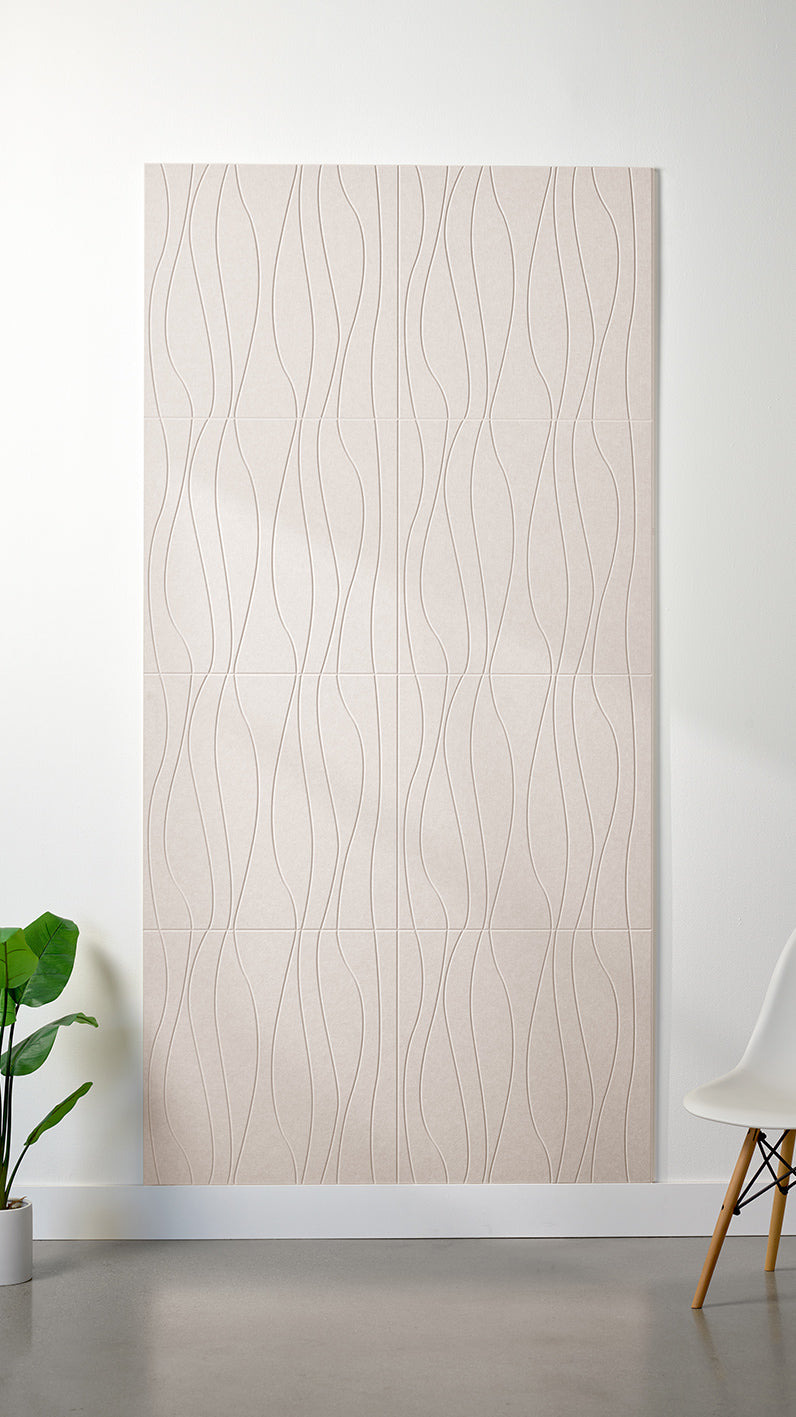 Heathered beige Felt Right 4’ x 8’ PET felt panel with flowing lines engraved into the material against a white wall. A plant and chair are in the foreground.