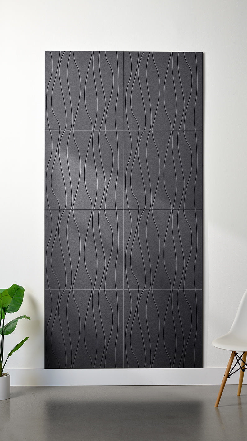Grey Felt Right 4’ x 8’ PET felt panel with flowing lines engraved into the material against a white wall. A plant and chair are in the foreground.