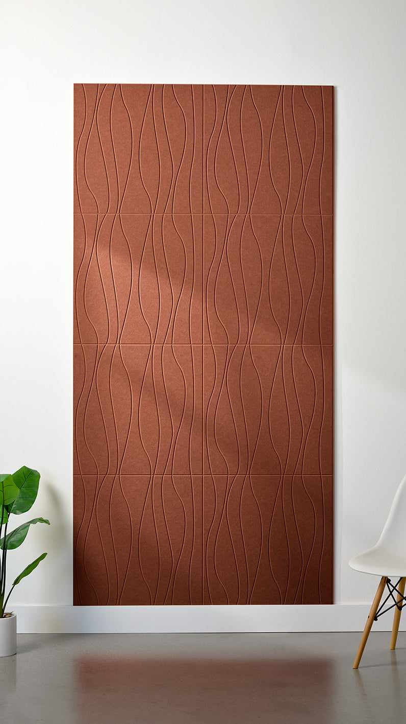 Burnt orange Felt Right 4’ x 8’ PET felt panel with flowing lines engraved into the material against a white wall. A plant and chair are in the foreground.