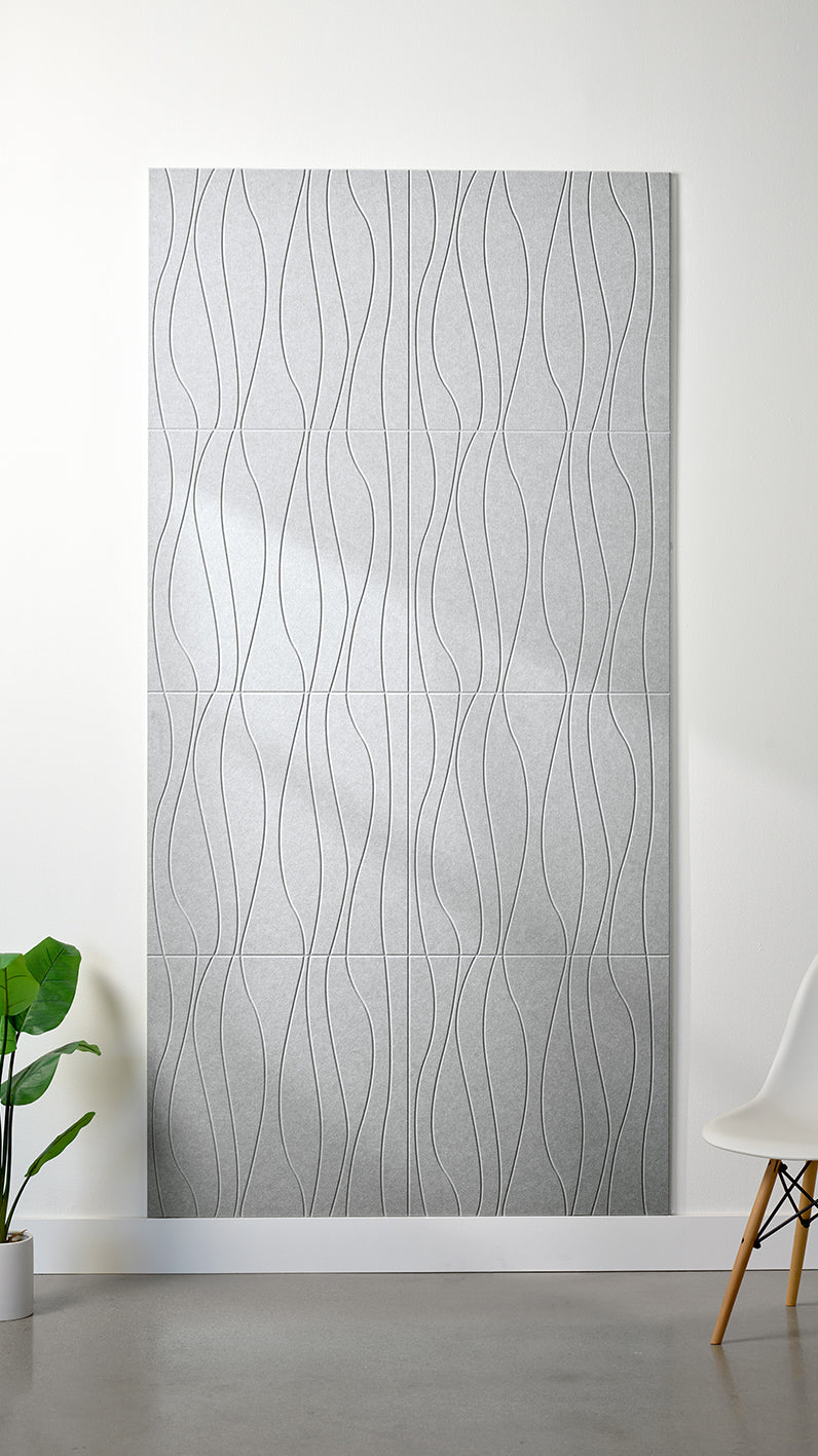 Heathered grey Felt Right 4’ x 8’ PET felt panel with flowing lines engraved into the material against a white wall. A plant and chair are in the foreground.