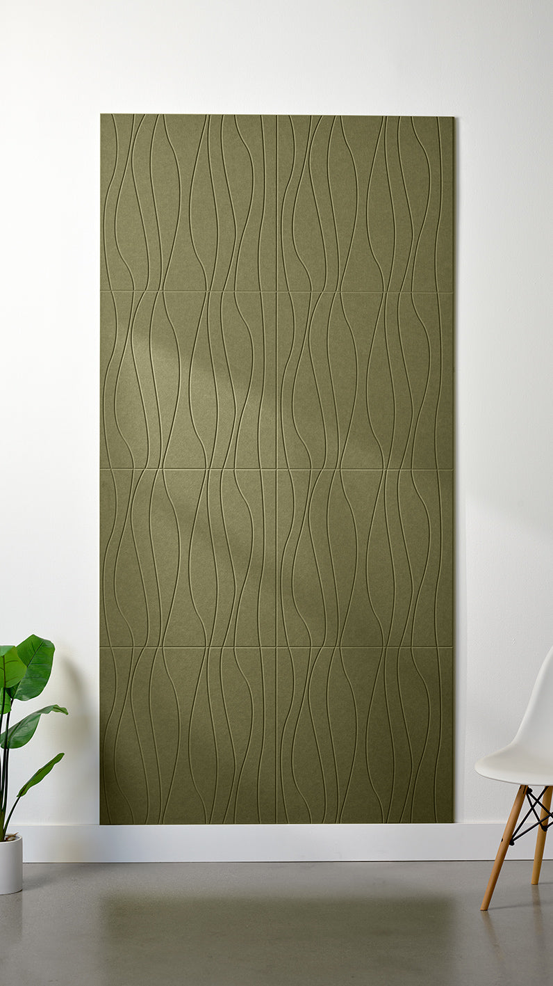 Olive green Felt Right 4’ x 8’ PET felt panel with flowing lines engraved into the material against a white wall. A plant and chair are in the foreground.