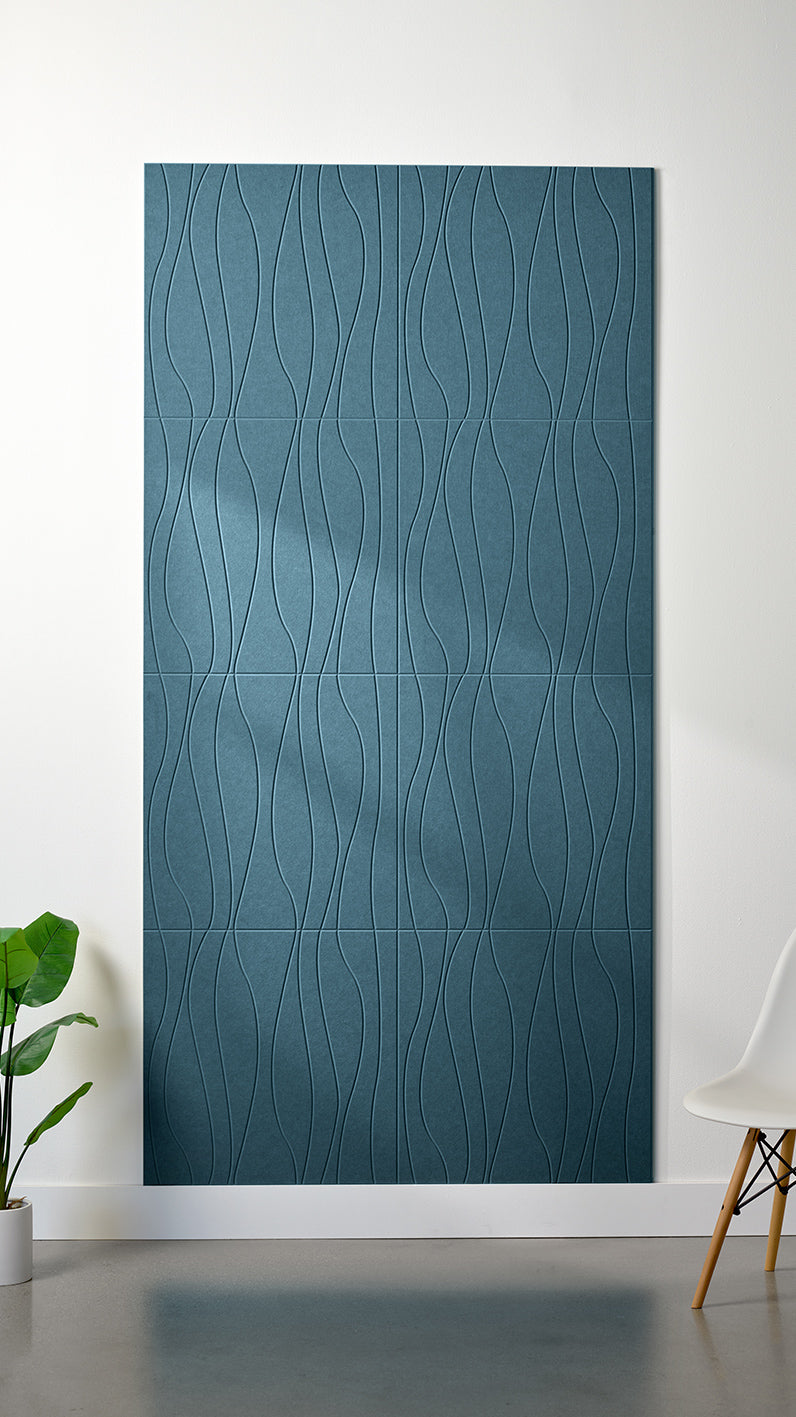 Blue Felt Right 4’ x 8’ PET felt panel with flowing lines engraved into the material against a white wall. A plant and chair are in the foreground.