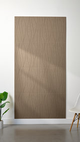 Light brown Felt Right 4’ x 8’ PET felt panel with flowing lines engraved into the material against a white wall. A plant and chair are in the foreground.