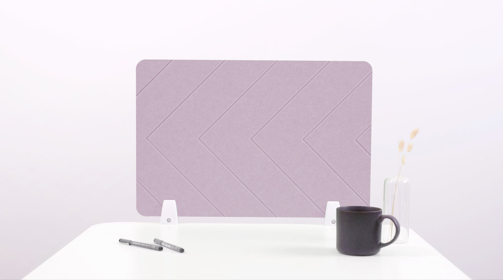 A lilac-colored felt desk divider placed on a desk with a pen and a mug on its surface.