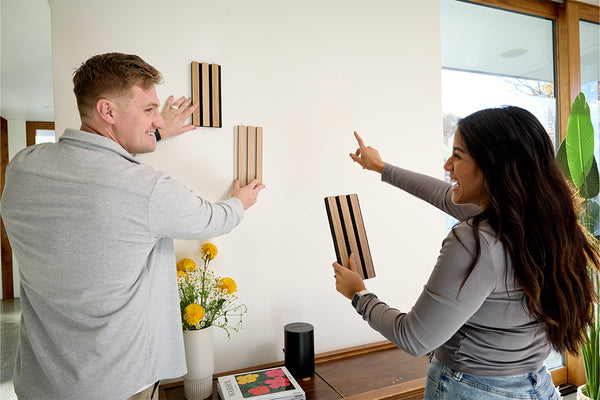 Two people holding and comparing wood slat samples with varying stain colors and finishes indoors.