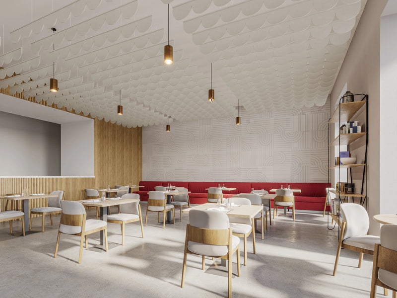 A modern dining room or cafe interior with multiple light wood chairs, white upholstered seats, and small round tables arranged in rows. A long red upholstered counter or sofa runs along one wall, and the ceiling has a textured white patterned design with hanging cylindrical pendant lights.