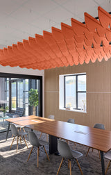 Orange scallop-shaped acoustic baffles suspended from white ceiling in modern office space above conference table.