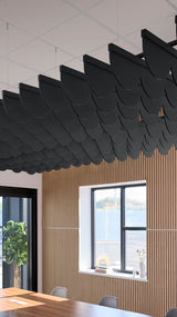 Black scalloped acoustic baffle suspended from ceiling above wood-paneled wall with window.