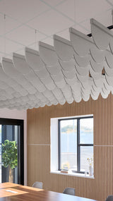 Gray scallop-shaped acoustic baffles suspended from ceiling in overlapping rows above wood-paneled wall with windows.